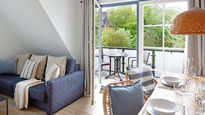 Ein modernes Wohnzimmer mit Sofa, Esstisch und Stühlen. Ein großes Fenster bietet einen Blick ins Freie.