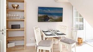 A dining area with a table set for four, white chairs, and a large painting of a beach scene on the wall.