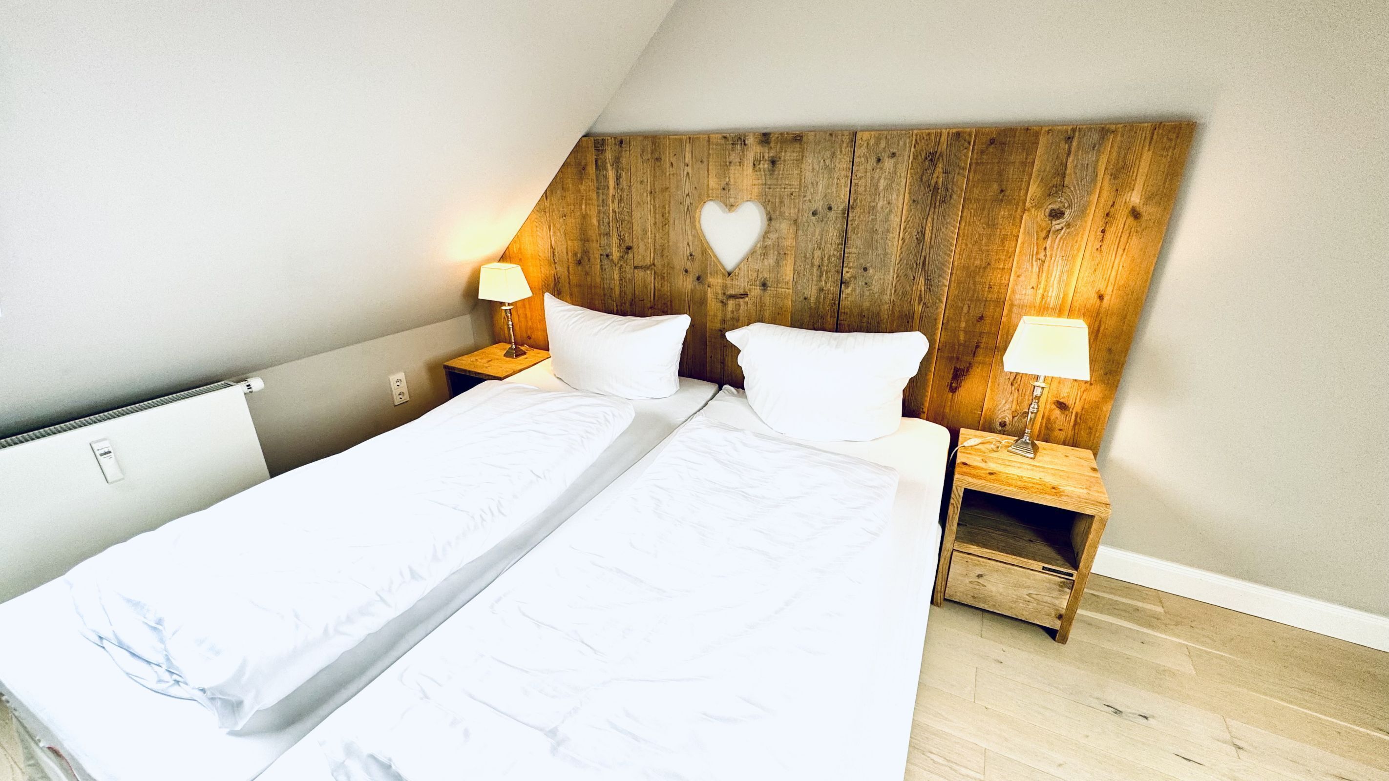 A bedroom with a wooden headboard, two bedside tables with lamps, and a heart-shaped cutout.