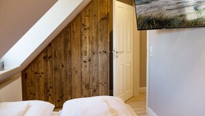 A bedroom with a sloped ceiling, wooden paneling, a white door, and a bed with white bedding.