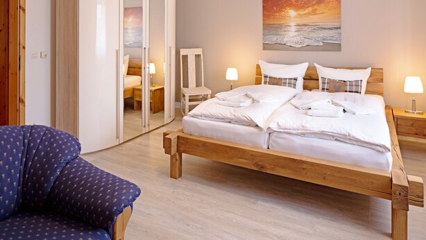 Un dormitorio con una cama de madera, una silla, un armario y un cuadro de una puesta de sol sobre el océano.