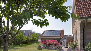 Una casa con techo solar, pared de piedra con flores y un jardín con un árbol.
