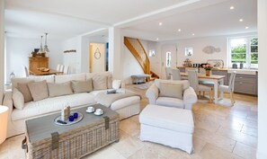 A spacious living area with a sofa, ottoman, and a dining table with chairs. A staircase leads to an upper level.