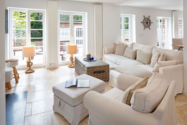 A spacious living room with a large white sofa, a small ottoman, and a wicker side table.