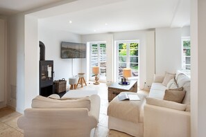A spacious living room with a fireplace, a television, and a view of the garden through large windows.