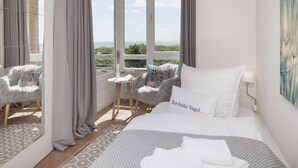 Ein Hotelzimmer mit Bett, Sessel, Meerblick und einem großen Fenster.