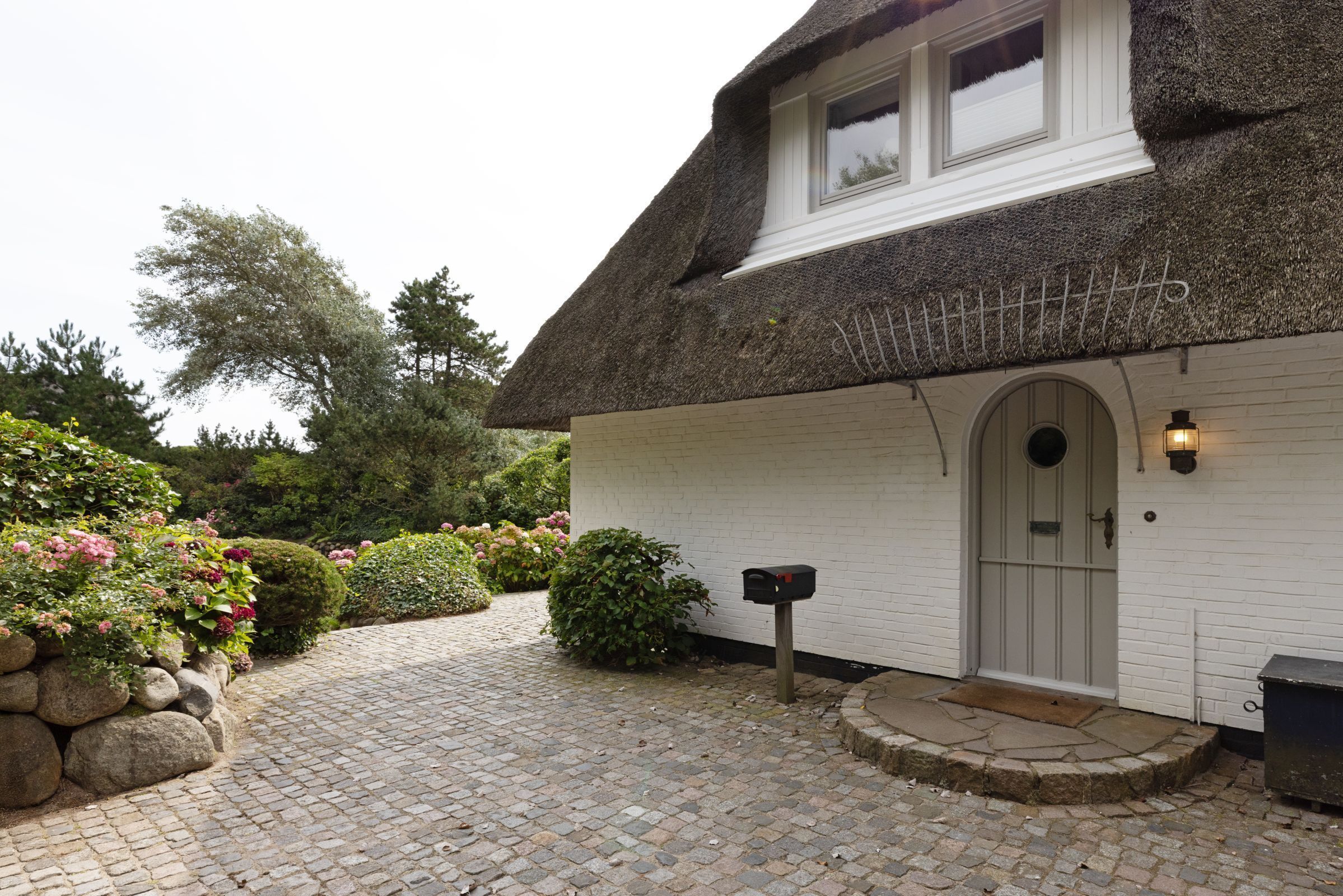 A traditional house with a thatched roof, a white brick exterior, and a mailbox.