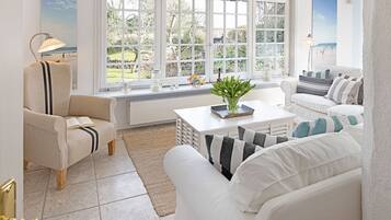 A bright living room with white furniture, large windows, and a view of the beach.