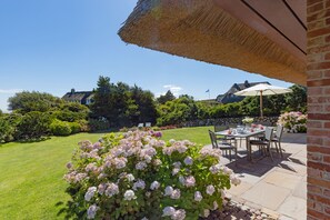 Eine Terrasse mit Tisch und Stühlen, umgeben von einem gepflegten Rasen und blühenden Pflanzen.