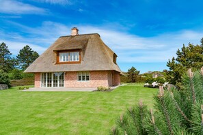Ein Haus mit Strohdach und Backsteinfassade, einem großen Fenster und einem gepflegten Rasen.