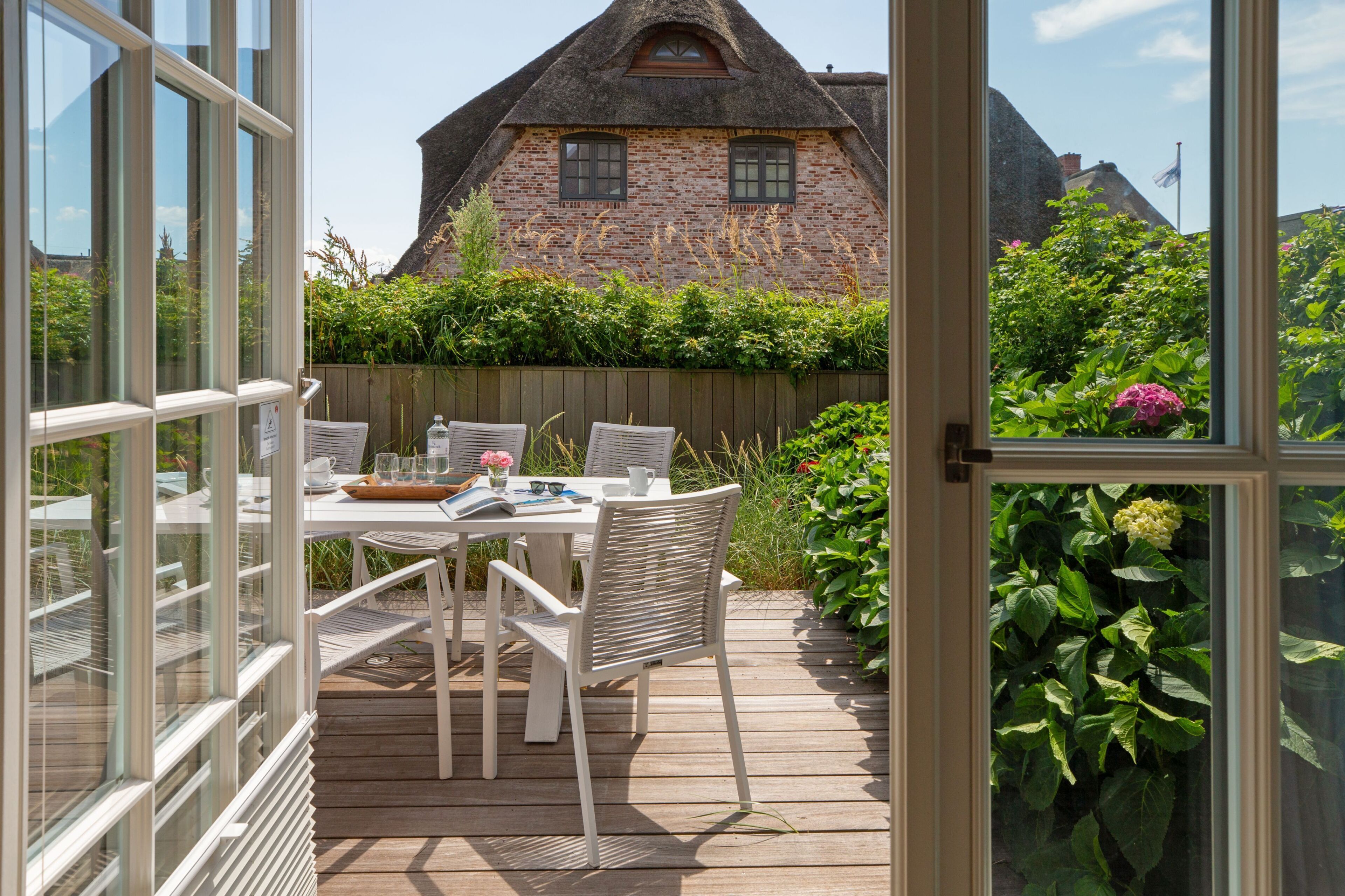 Une terrasse ouverte avec une table dressée pour deux personnes, d’où l’on peut admirer une maison en briques surmontée d’un toit de chaume.