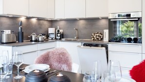 A modern kitchen with white cabinets, stainless steel appliances, and a dining area with a pink furry chair. - Herzlich Willkommen im Appartement Inseltraum (List)