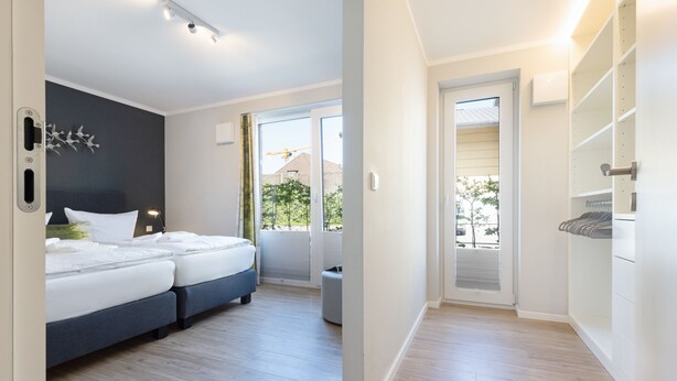 A modern bedroom with a large bed, a small seating area, and a view of the outdoors. - Herzlich Willkommen im Appartement Inseltraum (List)