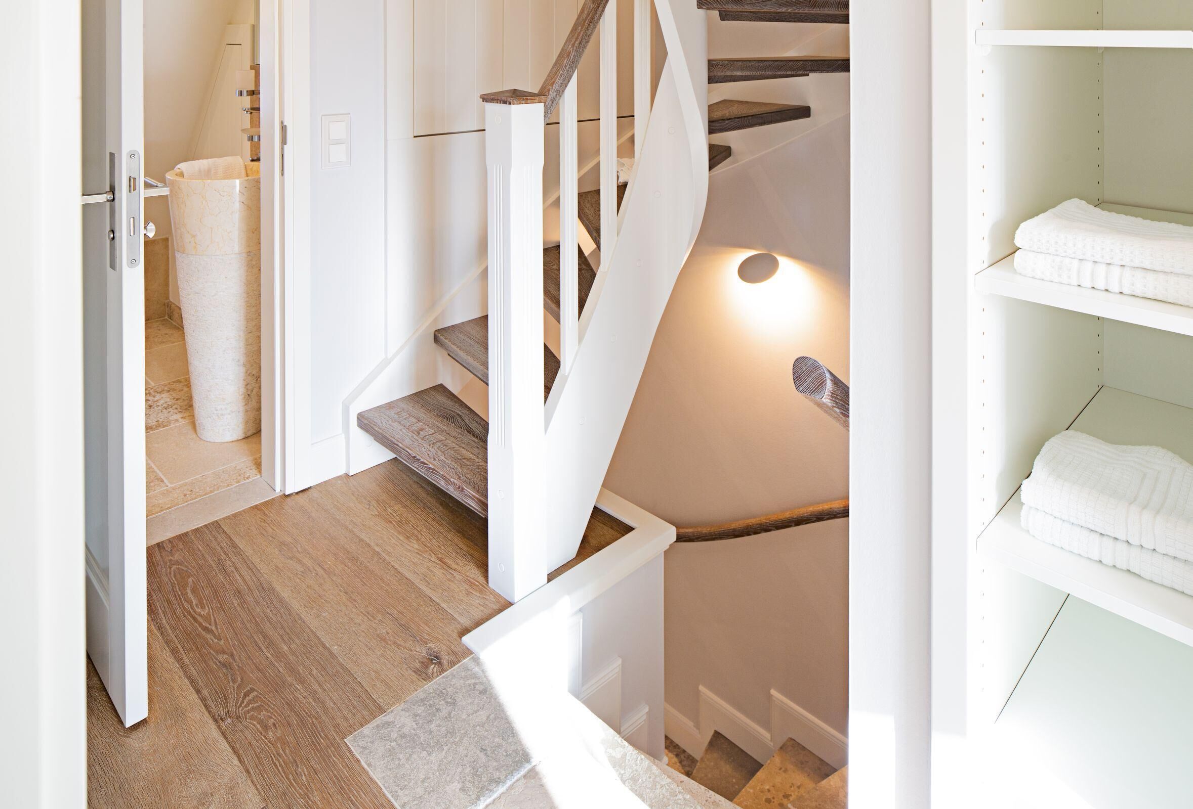 Een trap met houten treden en witte leuningen, die uitkomt op een plateau met een witte plank waar gevouwen handdoeken op liggen.