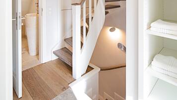 Een trap met houten treden en witte leuningen, die uitkomt op een plateau met een witte plank waar gevouwen handdoeken op liggen.