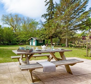 A picnic table set outdoors with a small green structure in the background.