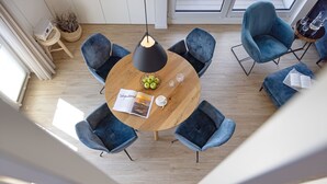 A modern dining area with a round wooden table surrounded by six blue chairs, a black pendant light, and a bowl of green apples. - Herzlich Willkommen im Appartement Meerzeit (List)