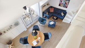 A modern living room with a blue sofa, a dining area with a round table, and a staircase. - Herzlich Willkommen im Appartement Meerzeit (List)
