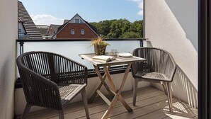 A balcony with two wicker chairs, a table with a book, a glass, and a basket. - Herzlich Willkommen im Appartement Meerzeit (List)