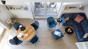 A modern living room with a round wooden table, blue chairs, a dark blue sofa, and a small side table with a lamp. - Herzlich Willkommen im Appartement Meerzeit (List)