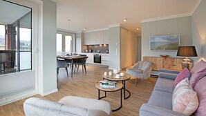 A modern living room with a grey sofa, a coffee table, and a dining area with a table and chairs. - Herzlich Willkommen im Appartement Priel (List)