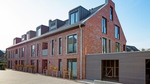 A modern brick building with multiple windows and a garage door. - Herzlich Willkommen im Appartement Priel (List)