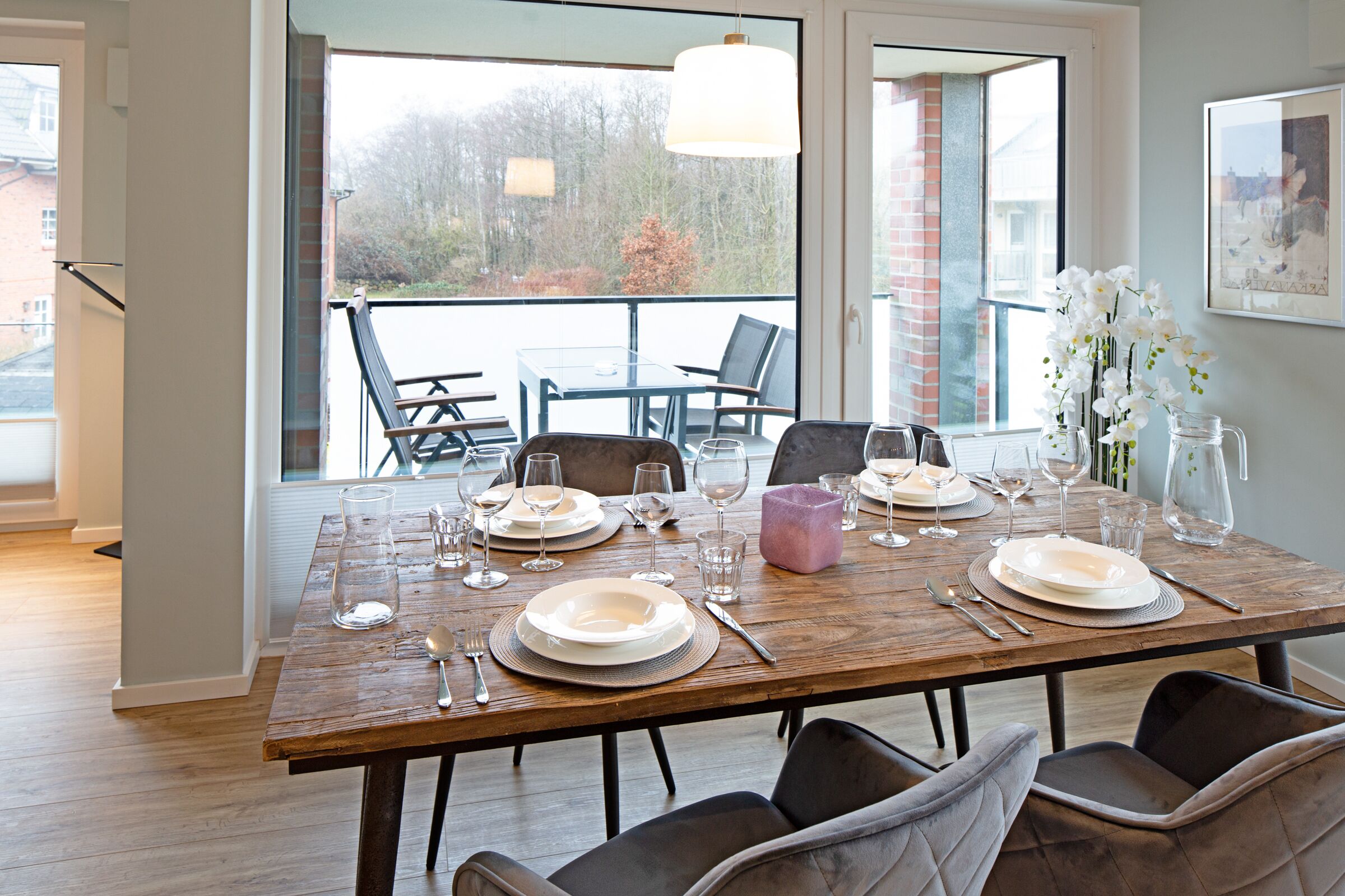Een eettafel gedekt met borden, glazen en bestek, met zicht op bomen en een balkon op de achtergrond.