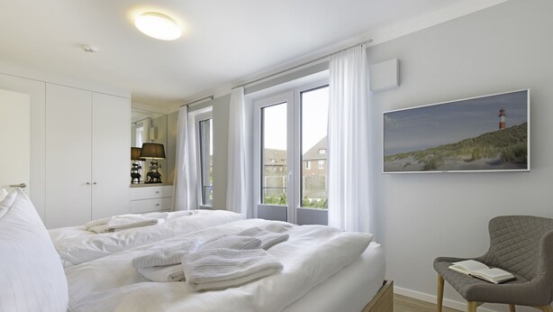 Ein Schlafzimmer mit einem großen Bett, einem Sessel, einem Gemälde und einem Fenster mit Vorhängen.