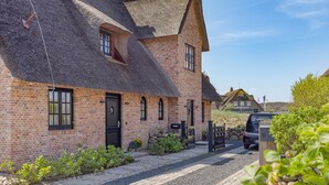 Ett traditionellt hus byggt av tegel med ett halmtak, en liten trädgård och en parkerad bil.