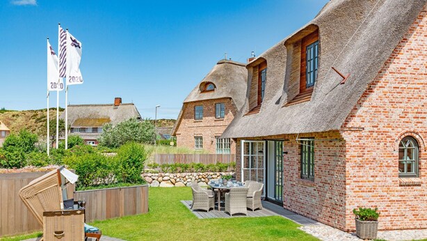 A thatched-roof house with a brick exterior, a wooden deck, and a patio table with chairs. - Herzlich Willkommen im Ferienhaus Trauminsel (List)