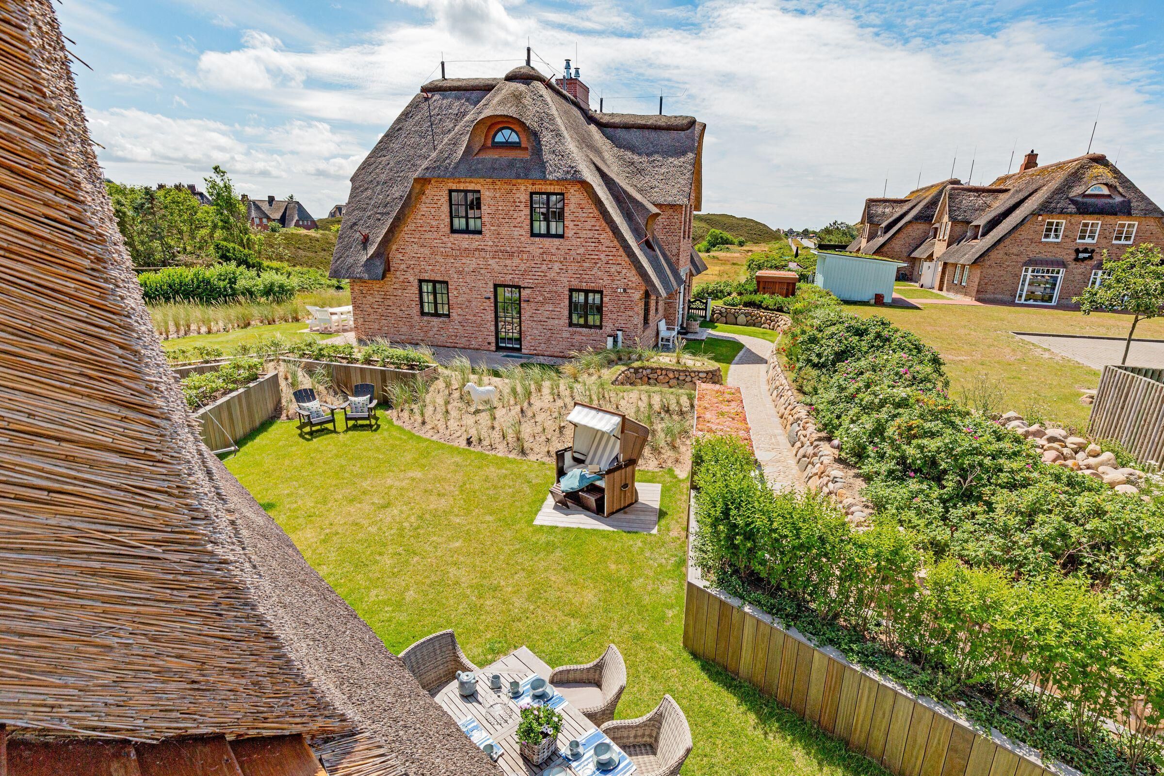 A large brick house with a thatched roof, a well-maintained lawn, and outdoor furniture.