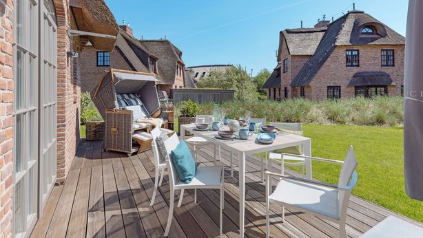 Een houten terras met een eettafel, omringd door witte stoelen.