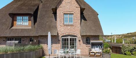 A large house with a steeply pitched thatched roof, brick walls, and a large front door.