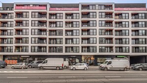 A multi-story building with balconies, a storefront, and parked vehicles. - RentPlanet - Apartament Wyszyńskiego (Wroclaw)