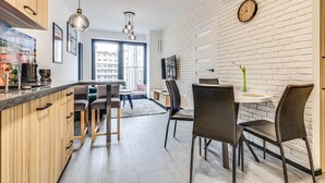 A modern kitchen with wooden cabinets, a dining area with chairs, and a white brick wall. - RentPlanet - Apartament Wyszyńskiego (Wroclaw)