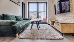 A modern living room with a green sofa, a round table, and a wooden cabinet. - RentPlanet - Apartament Wyszyńskiego (Wroclaw)