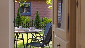 An open door to a room with a table set for two, a chair, and a view of a brick building with a window and a small tree.