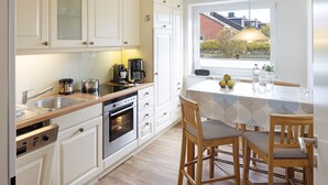 A modern kitchen with white cabinets, a wooden countertop, and a built-in oven. There is a dining area with a table and chairs, and a window with a view of the outside.