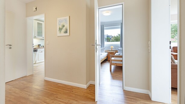 A spacious hallway with wooden flooring leading to a bedroom with a bed and a window.