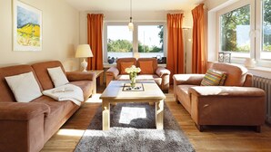 A modern living room with a sofa set, a coffee table, and a view of a body of water through large windows.