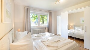 A bedroom with a large bed, a bedside table with a lamp, a window with curtains, and a wardrobe with a mirror.