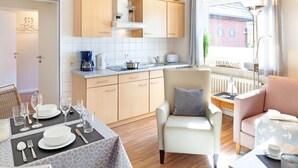 Una cocina moderna con armarios de madera, una mesa de comedor lista para cuatro personas y una zona de estar acogedora con sofá y sillón.