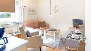 Una sala de estar moderna con sofá, mesa de centro y comedor. Hay un televisor, una ventana con persianas y un letrero en la pared.