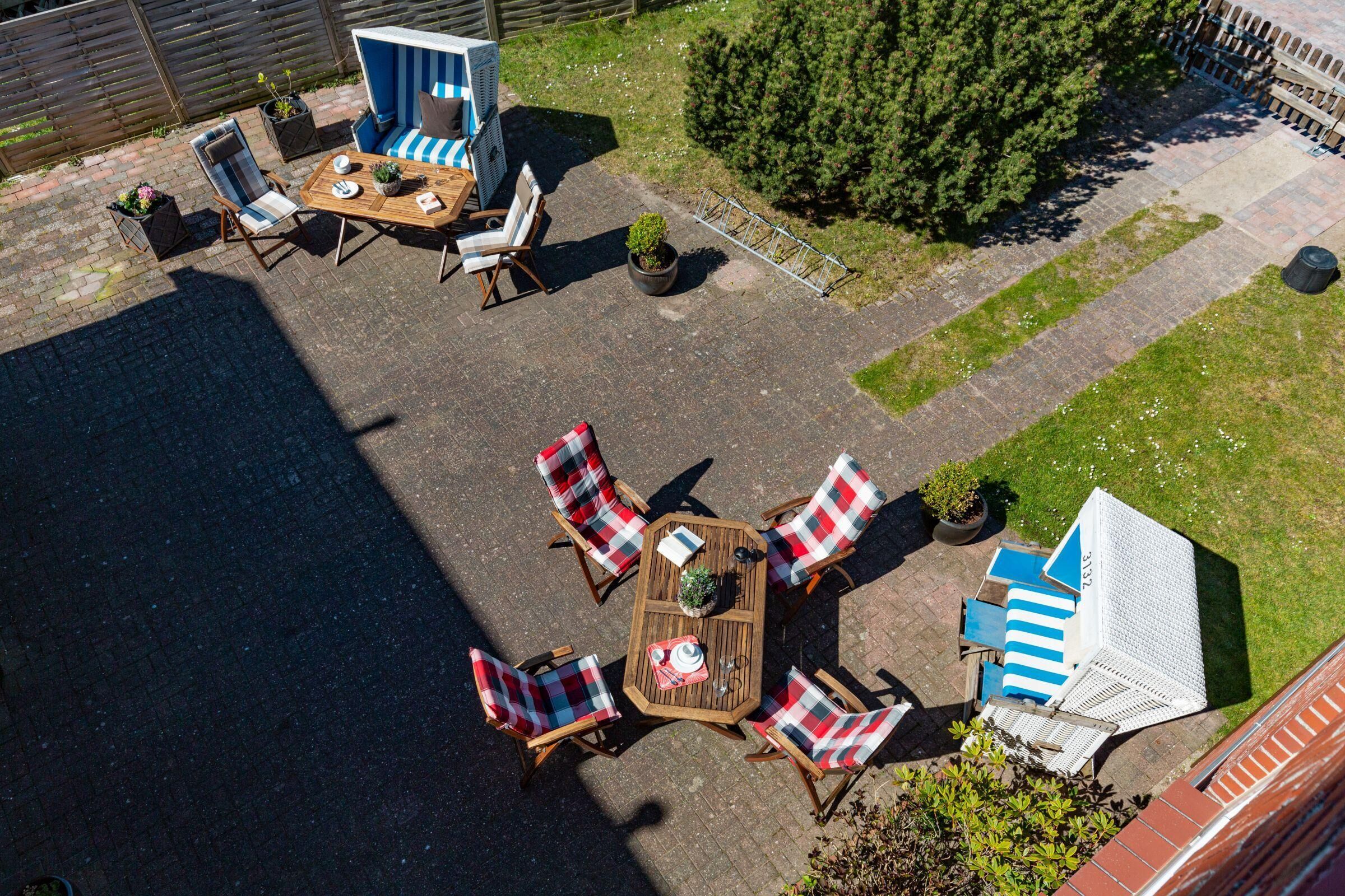 Een terras met een ronde houten tafel omringd door zes stoelen met gestreepte kussens, een blauwe en witte buitenbank en een kleine witte pergola.