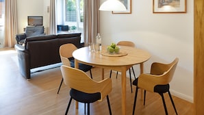 A modern living room with a sofa, a dining table with chairs, a TV, and a window with curtains. - Herzlich Willkommen im Appartement Koje (List)