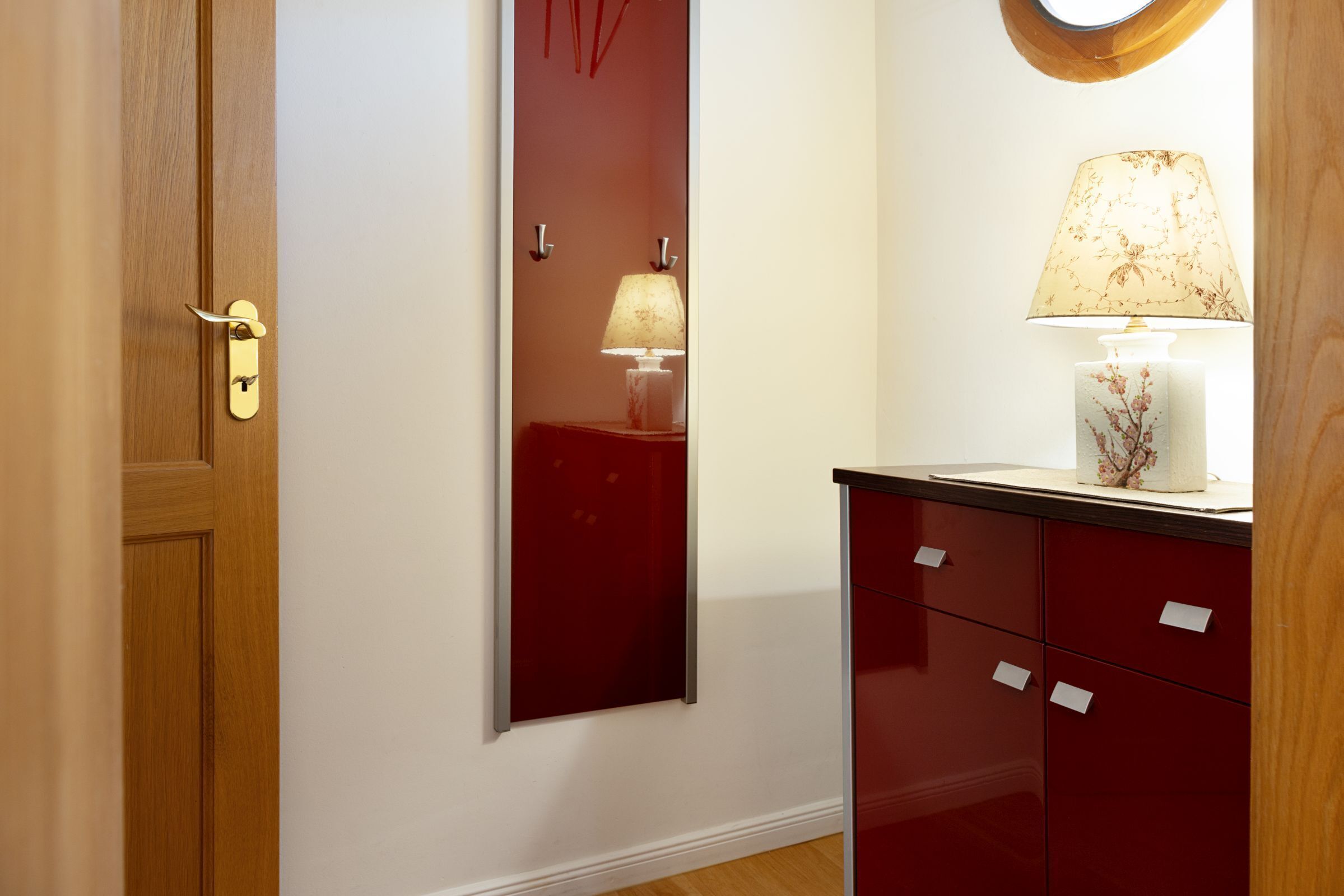 Um corredor com uma porta de madeira, um armário vermelho e uma luminária na parede.
