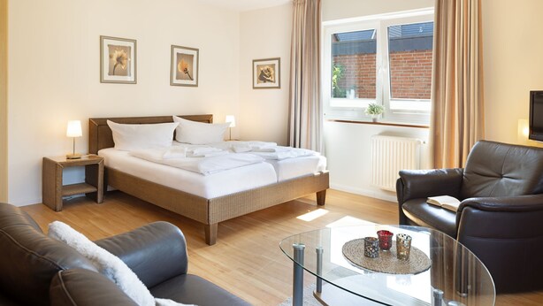 A modern hotel room with a large bed, a glass coffee table, leather sofas, and a view of a brick building through the window. - Herzlich Willkommen im Appartement Koje (List)