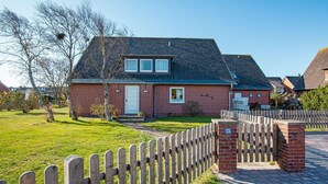 A brick house with a white door, a small front yard, and a wooden fence. - Herzlich Willkommen im Appartement Koje (List)