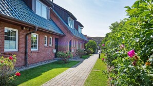 A row of brick houses with a paved walkway, a stone wall, and flowering bushes. - Herzlich Willkommen im Ferienhaus Olivia (List)