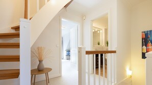 A staircase with wooden steps and white railings, leading to a room with a white door and a small table with a vase. - Herzlich Willkommen im Ferienhaus Olivia (List)